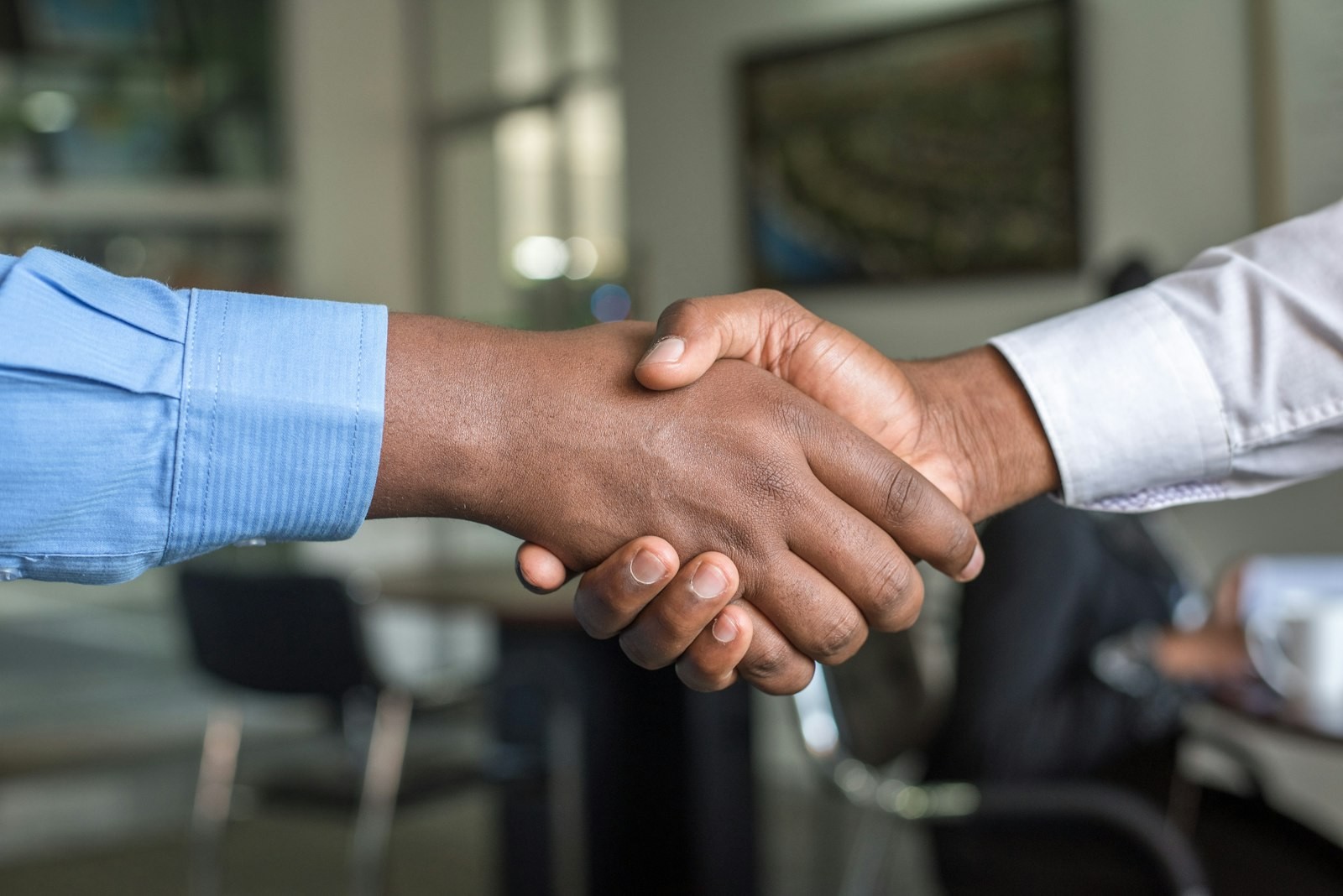 Two business professionals shaking hands in a modern office, symbolising a people-first partnership and the principle of liberating capacity rather than reducing headcount